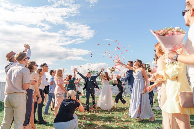 Wedding guests throwing confetti over the newlyweds in bright daylight